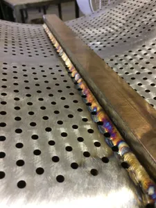 Close-up of a TIG weld joining a stainless stiffener bar to a perforated stainless screen