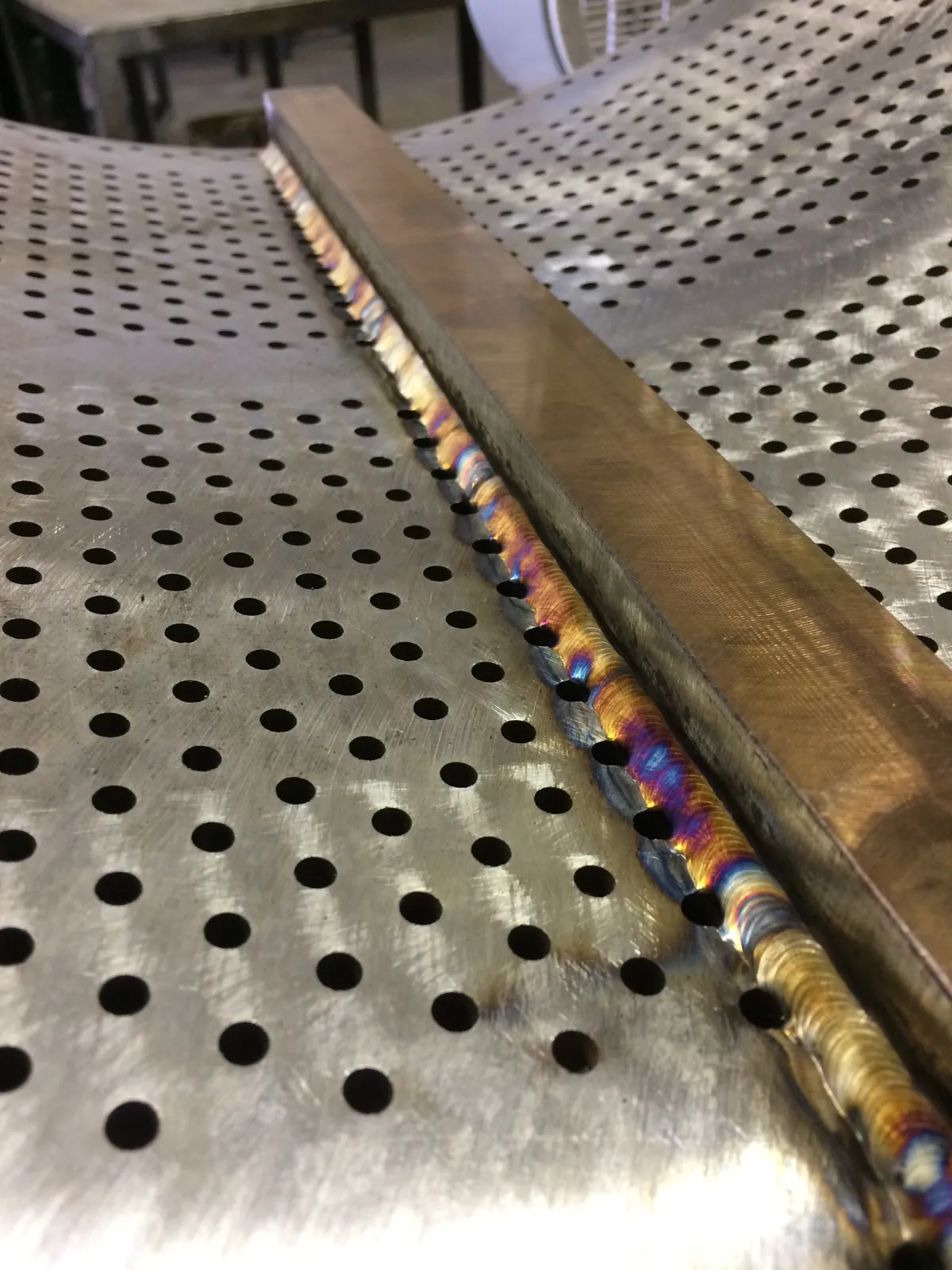 Close-up of a TIG weld joining a stainless stiffener bar to a perforated stainless screen