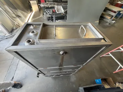 Fabricated stainless steel tank enclosure with welded ports and a lid, on the shop floor